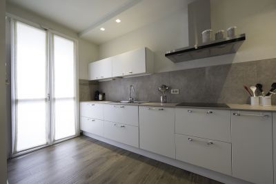 Helle Küche mit Holzoptik-Bodenfliesen und grauen Fliesen als Spritzschutz.