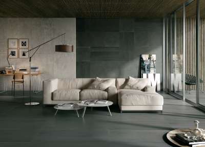 Großzügiges Wohnzimmer mit dunklen Porcelaingres Fliesen an Boden und Wand, hellem Sofa.