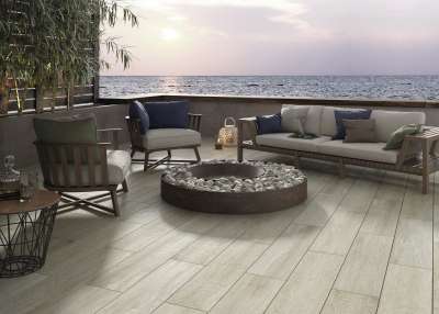 Terrasse mit hellen Holzoptik-Fliesen, Lounge-Sofa und Meerblick bei Sonnenuntergang.