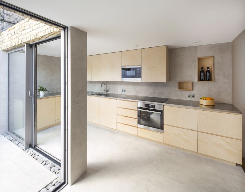 Moderne Küche mit grauen Betonoptik-Fliesen und hellem Holz, offener Übergang zum Außenbereich.