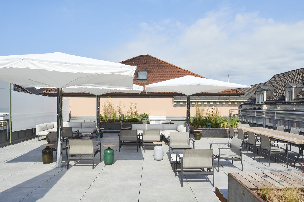 Helle, moderne Dachterrasse mit hochwertigen Outdoor-Fliesen, Loungemöbeln und Sonnenschirmen.