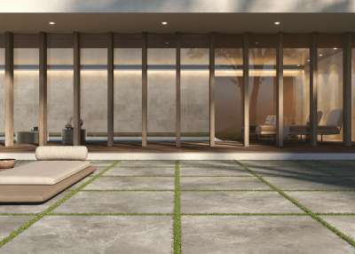 Großformatige graue Terrassenfliesen mit Grünfugen vor einem modernen Glaspavillon.