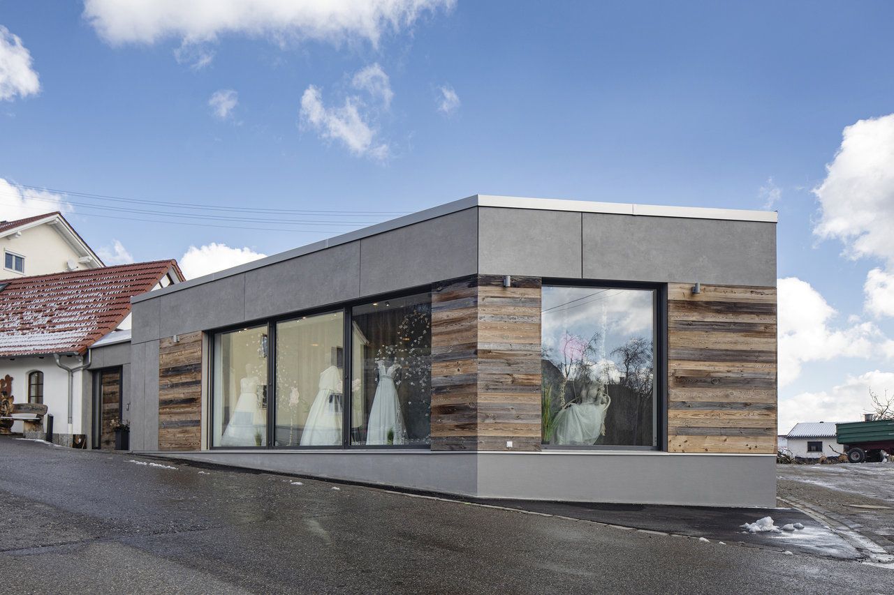 Modernes Gebäude mit grauer Fassade und Holzverkleidung, in den Schaufenstern sind Brautkleider zu sehen.