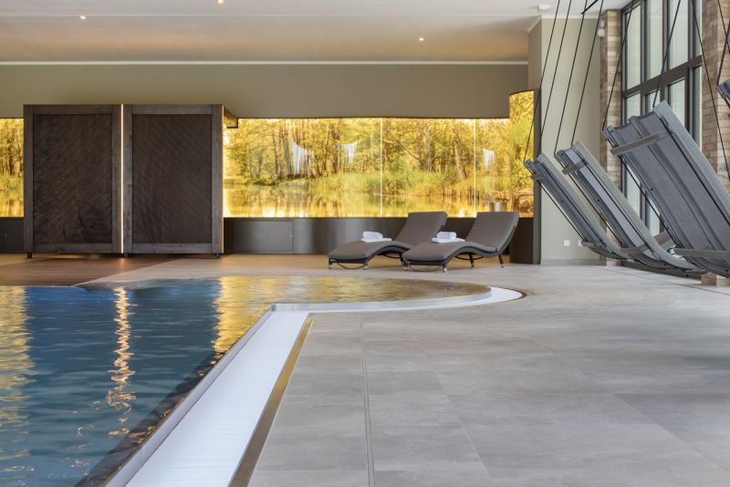 Indoor-Poolbereich mit eleganten hellgrauen Fliesen und bequemen Liegen.