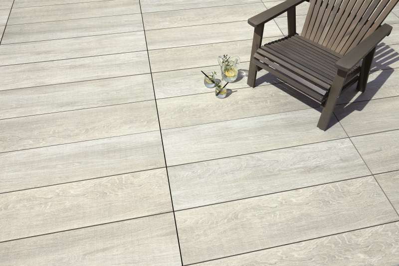 Terrassenfliesen in heller Holzoptik mit Stuhl und Gläsern.