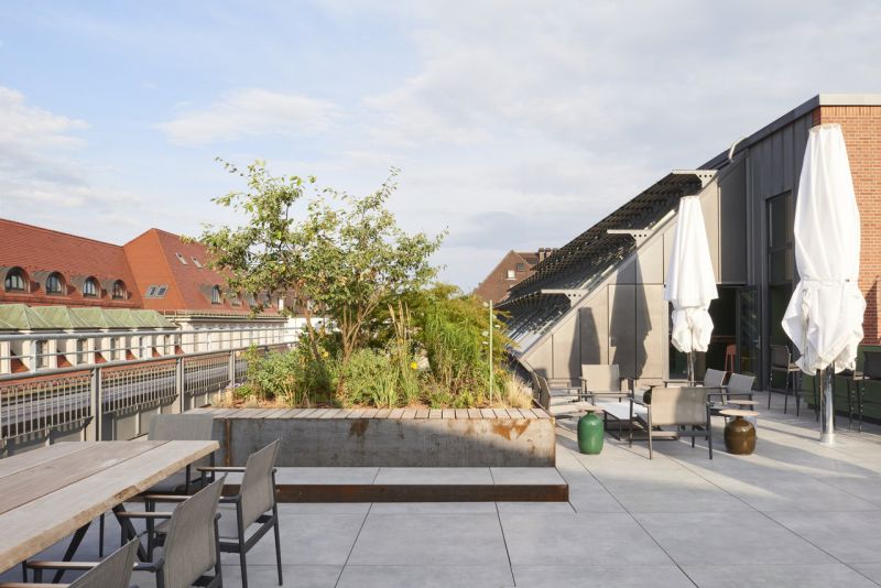Moderne Dachterrasse mit hellgrauen Outdoor-Fliesen, Pflanzen und verschiedenen Sitzbereichen.
