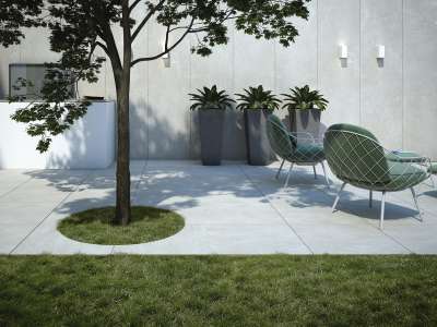 Moderne Terrasse mit hellgrauen Outdoor-Fliesen, Baum, Pflanzen und stilvollen Sitzmöbeln.