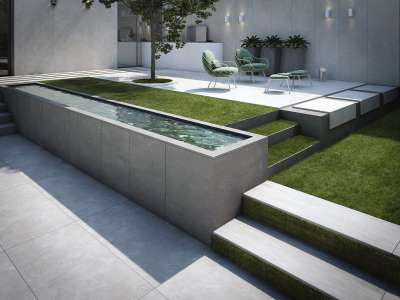 Graue Outdoor-Fliesen auf einer modernen, mehrstufigen Terrasse mit Wasserelement und Grünflächen.