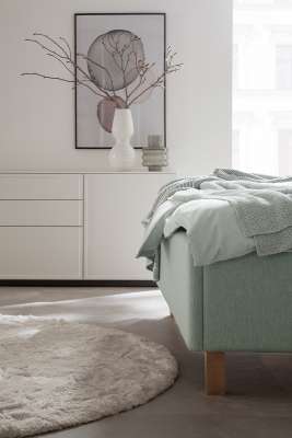 Modernes Schlafzimmer mit dunklen Bodenfliesen, hellgrünem Boxspringbett und minimalistischer Deko.