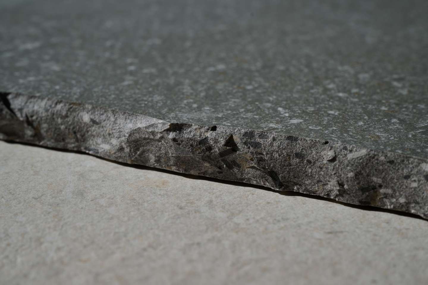 Bruchraue Kante einer anthrazitfarbenen Fliese mit strukturierter Oberfläche.