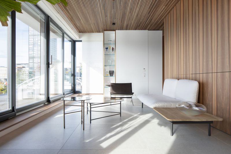 Moderner Wohnbereich mit Porcelaingres Fliesen in Hellgrau, Holzdecke und großen Fenstern.