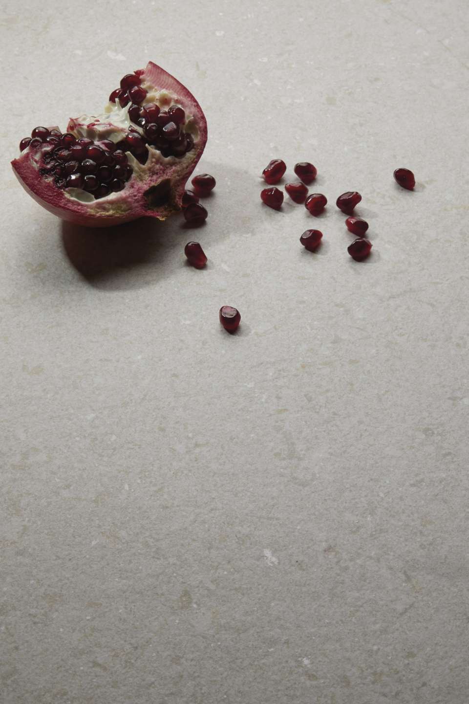 Granatapfelhälfte und einzelne Kerne auf hellgrauer, strukturierter Fliese.