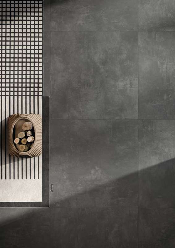 Dunkelgraue Betonoptik-Fliesen mit grafischem Muster und Kaminholzkorb.