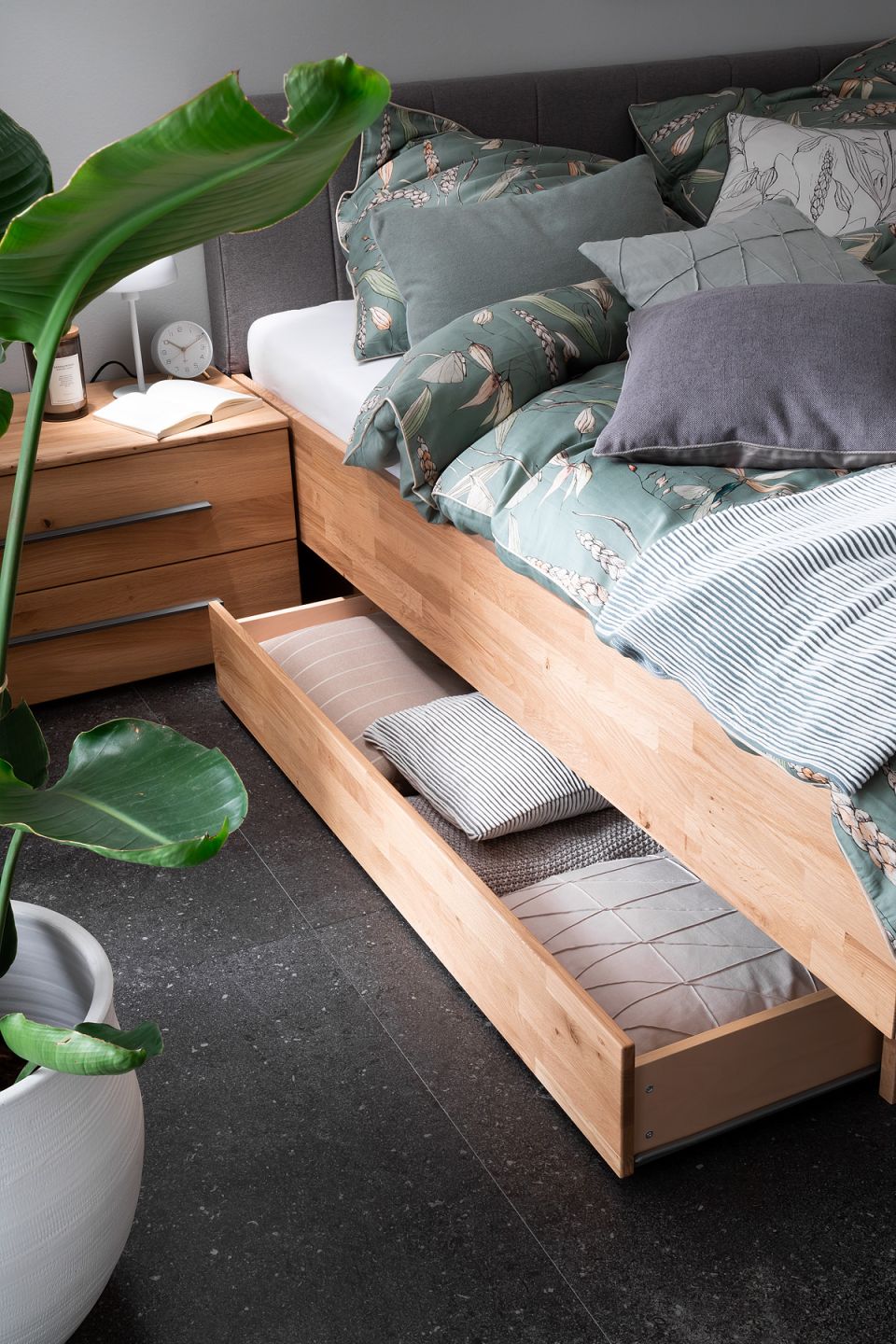 Modernes Schlafzimmer mit dunklen Fliesen als Bodenbelag, Holzbett und grüner Bettwäsche.