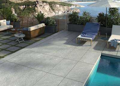 Hochwertige Outdoor-Fliesen in hellem Grau auf einer Terrasse mit Meerblick und Pool.