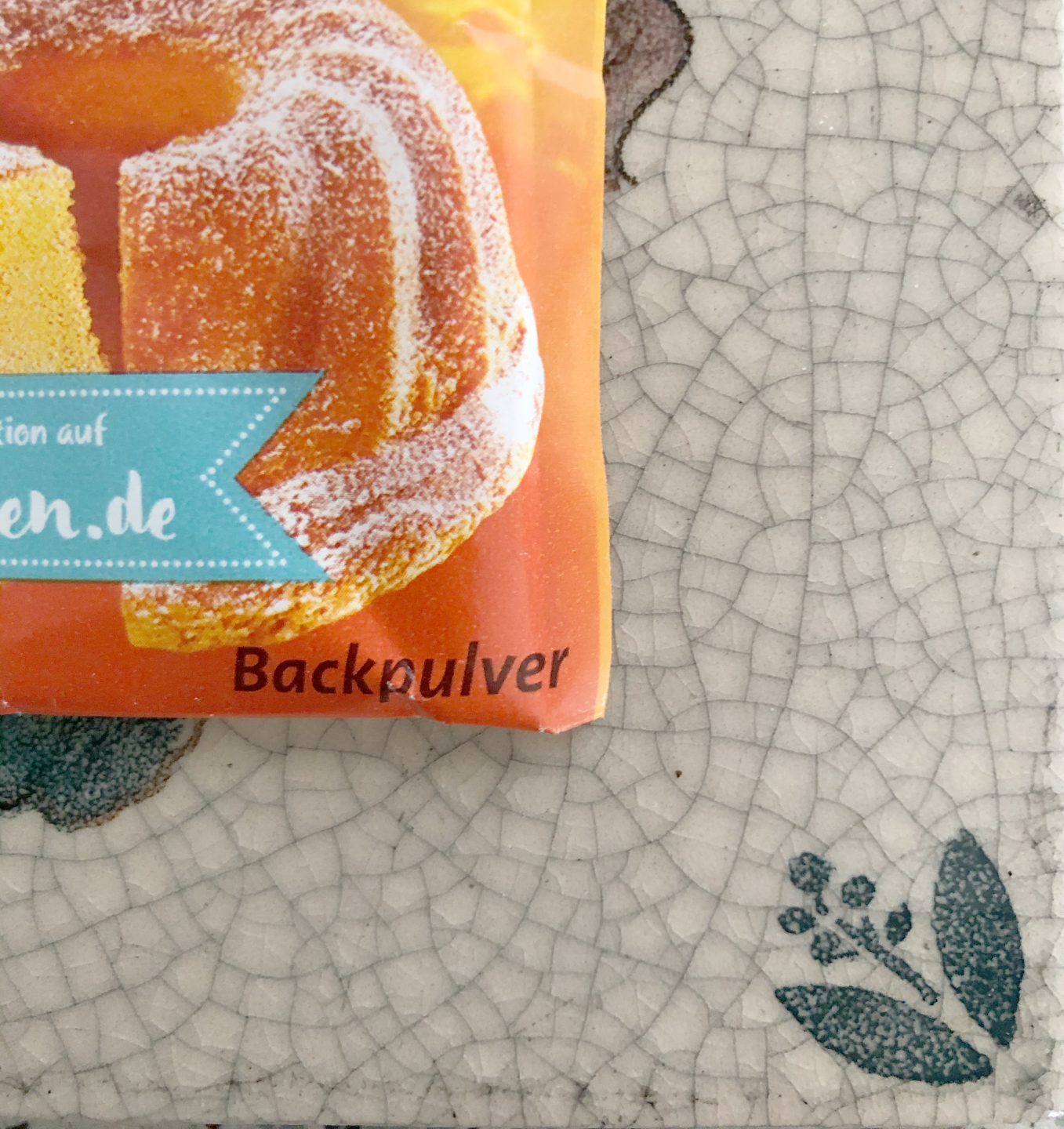 Orangefarbene, gezuckerte Fruchtstücke mit blauem Etikett auf hellem, gemustertem Untergrund.