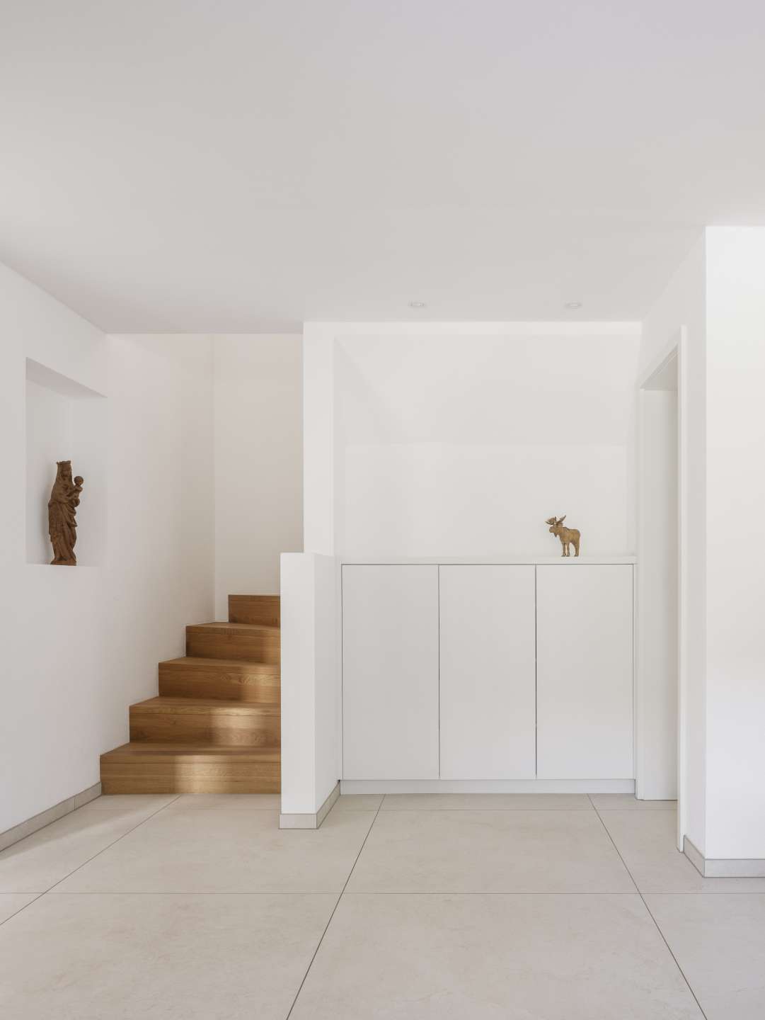 Heller, moderner Raum mit großformatigen Bodenfliesen und Holztreppe.