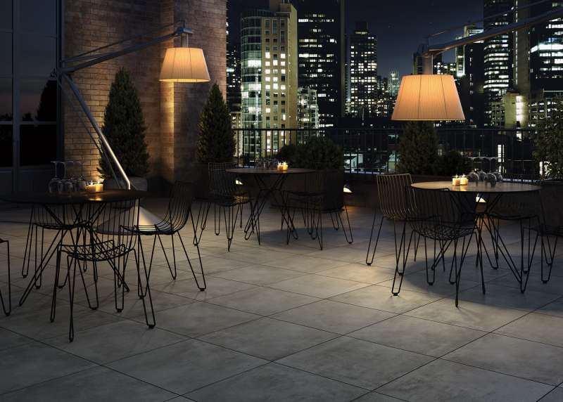 Elegante Dachterrasse mit hochwertigen Outdoor-Fliesen, stilvollen Möbeln und nächtlichem Stadtpanorama.