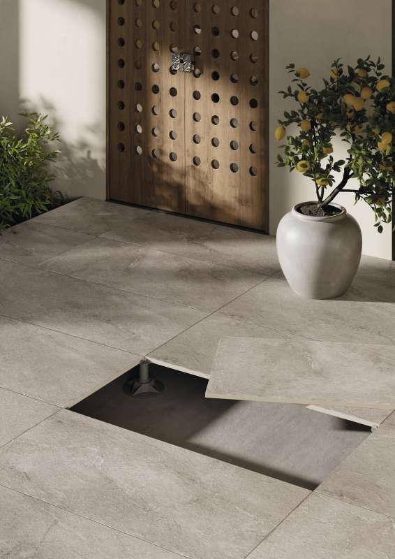 Graue Outdoor-Fliesen auf Stelzlagern, eine Fliese angehoben zeigt das Entwässerungssystem.