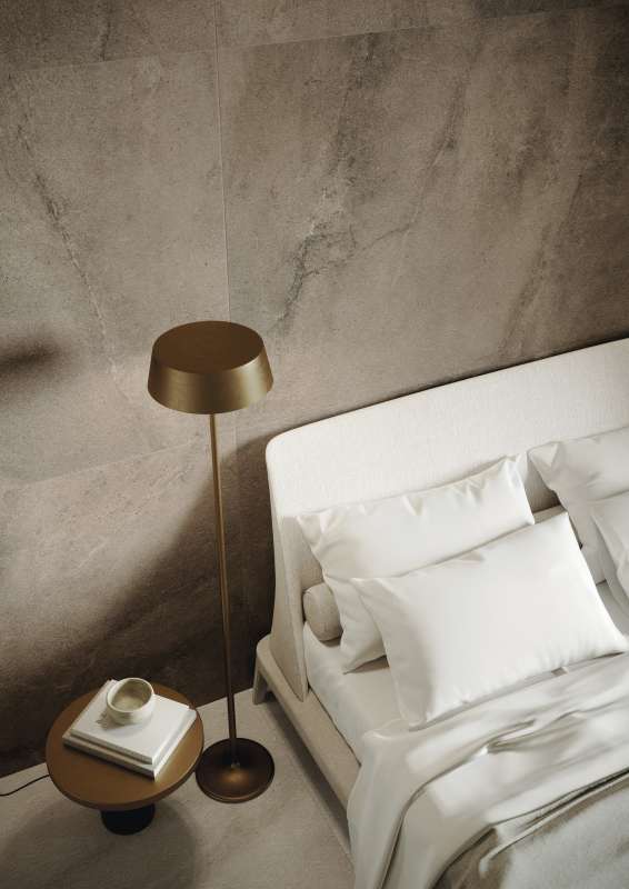 Schlafzimmer mit Porcelaingres Wandfliesen in Natursteinoptik, einem Bett und Designer-Stehlampe.